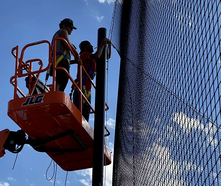 Two Construction Workers Hanging Netting on a Sports Field